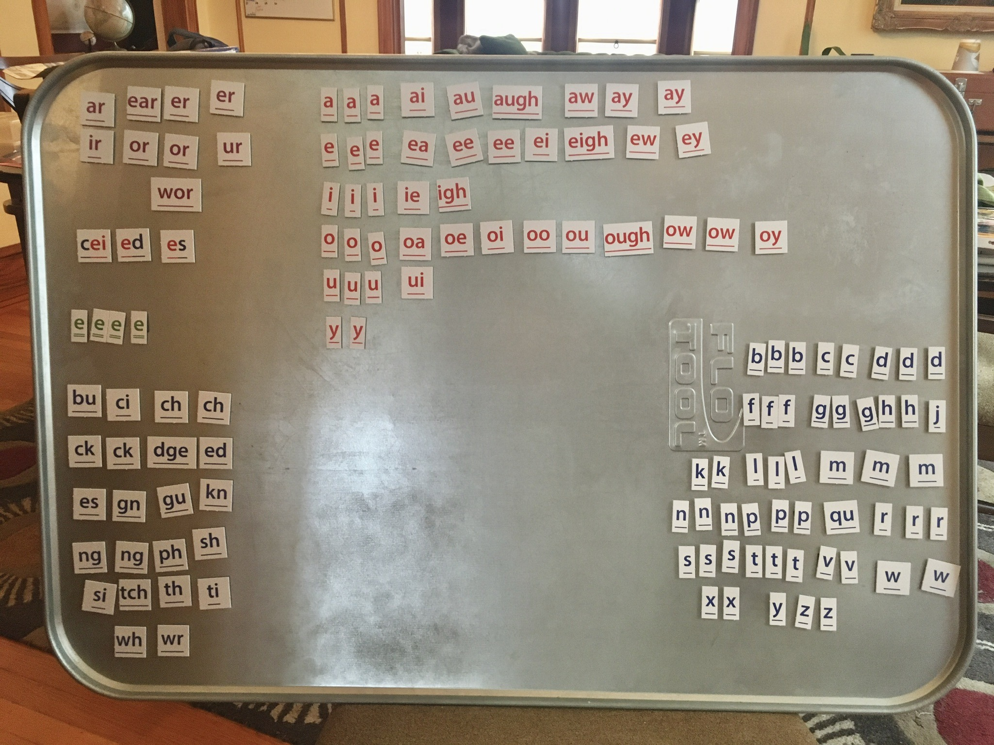 White tiles with letters and letter groups (phonograms) arranged on a large metal tray.