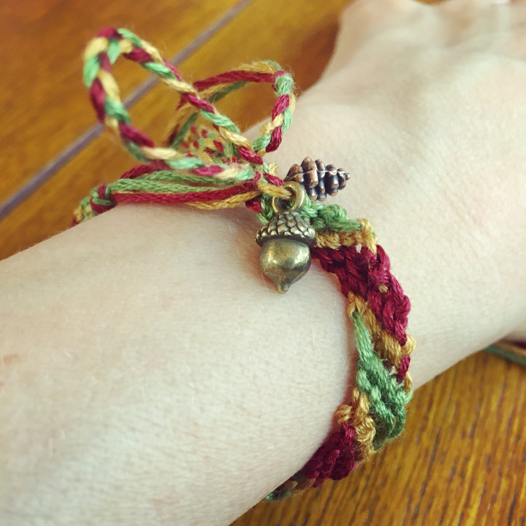 A friendship bracelet made from embroidery floss, with a small metal acorn charm