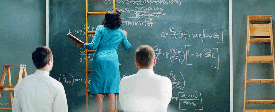 A scene from the film Hidden Figures, with mathematician Katherine Johnson writing equations on a chalkboard as two colleagues look on.