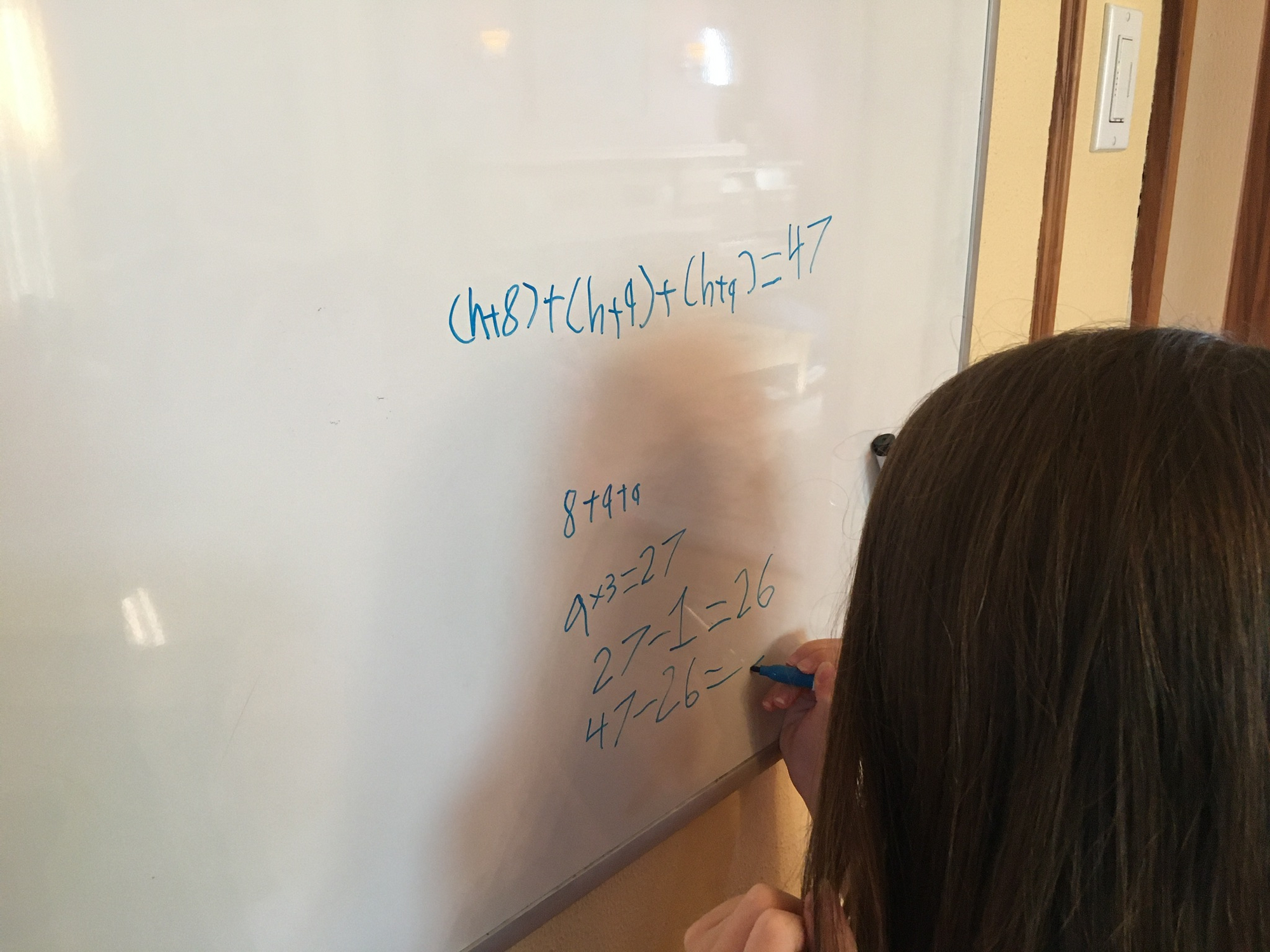Wanda standing at a large whiteboard, writing out a math problem.