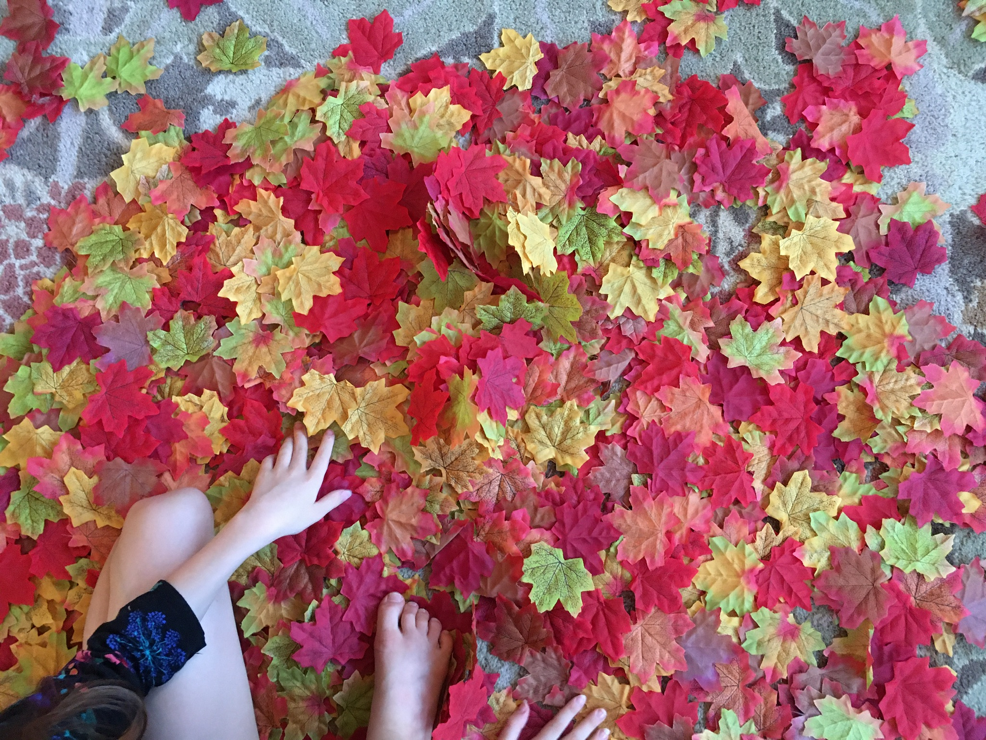 Fake fall maple leaves made of fabric in red, orange, yellow, green, and brown, in a pile.