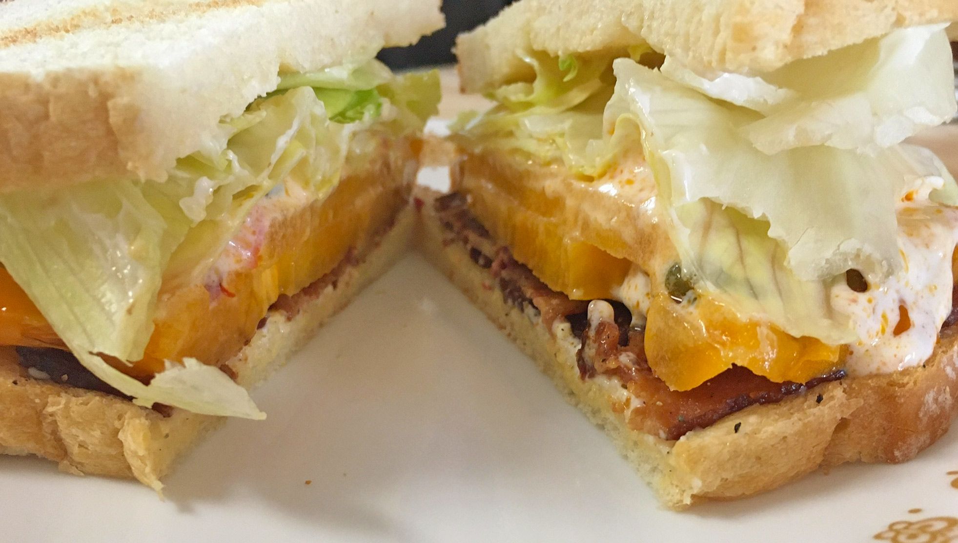 A sandwich is on a plate, with bacon, yellow tomato, and lettuce.