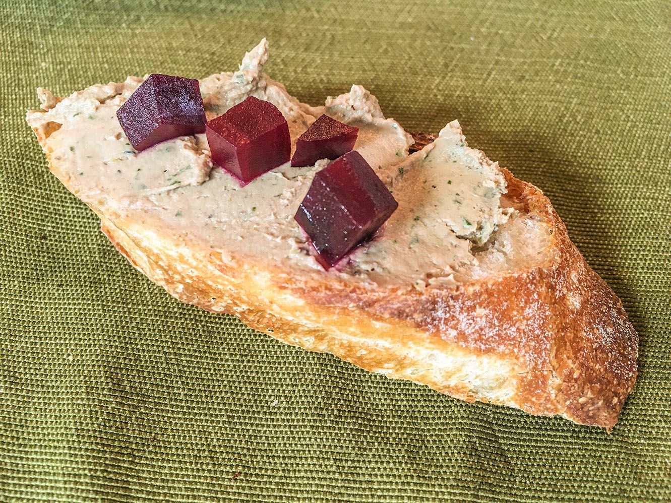 A slice of baguette, topped with pâté and small deep red cubes of pickled beets.
