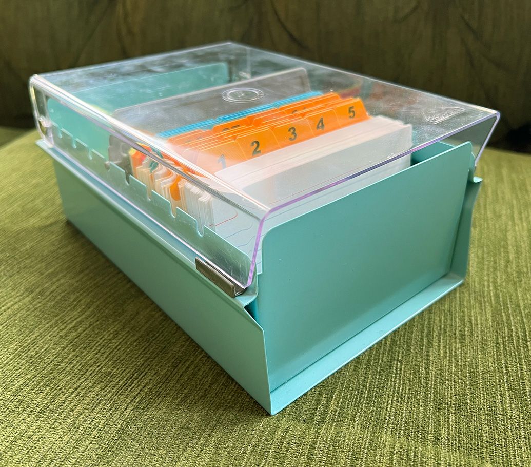 An index card organizing box, with a metal base and a clear plastic lid. Inside are tabbed dividers.