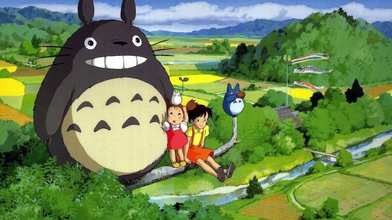 A scene from My Neighbor Totoro, with Totoro and the girls on a branch in a high tree overlooking rice fields.