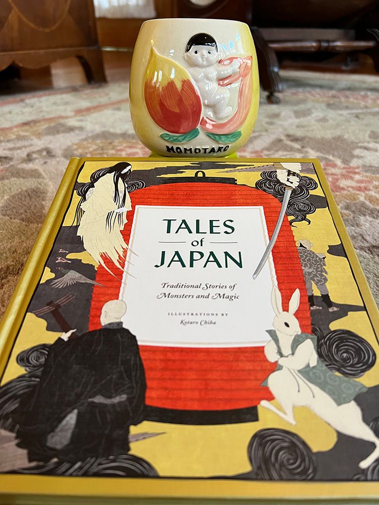 The cover of the book Tales of Japan, with elegant character drawings, and a ceramic mug with a baby coming out of a peach.