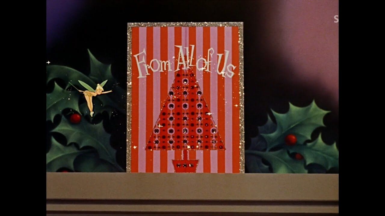 Tinkerbell hovers next to the front of a pink and red Christmas card with the words "From All of Us" in white.