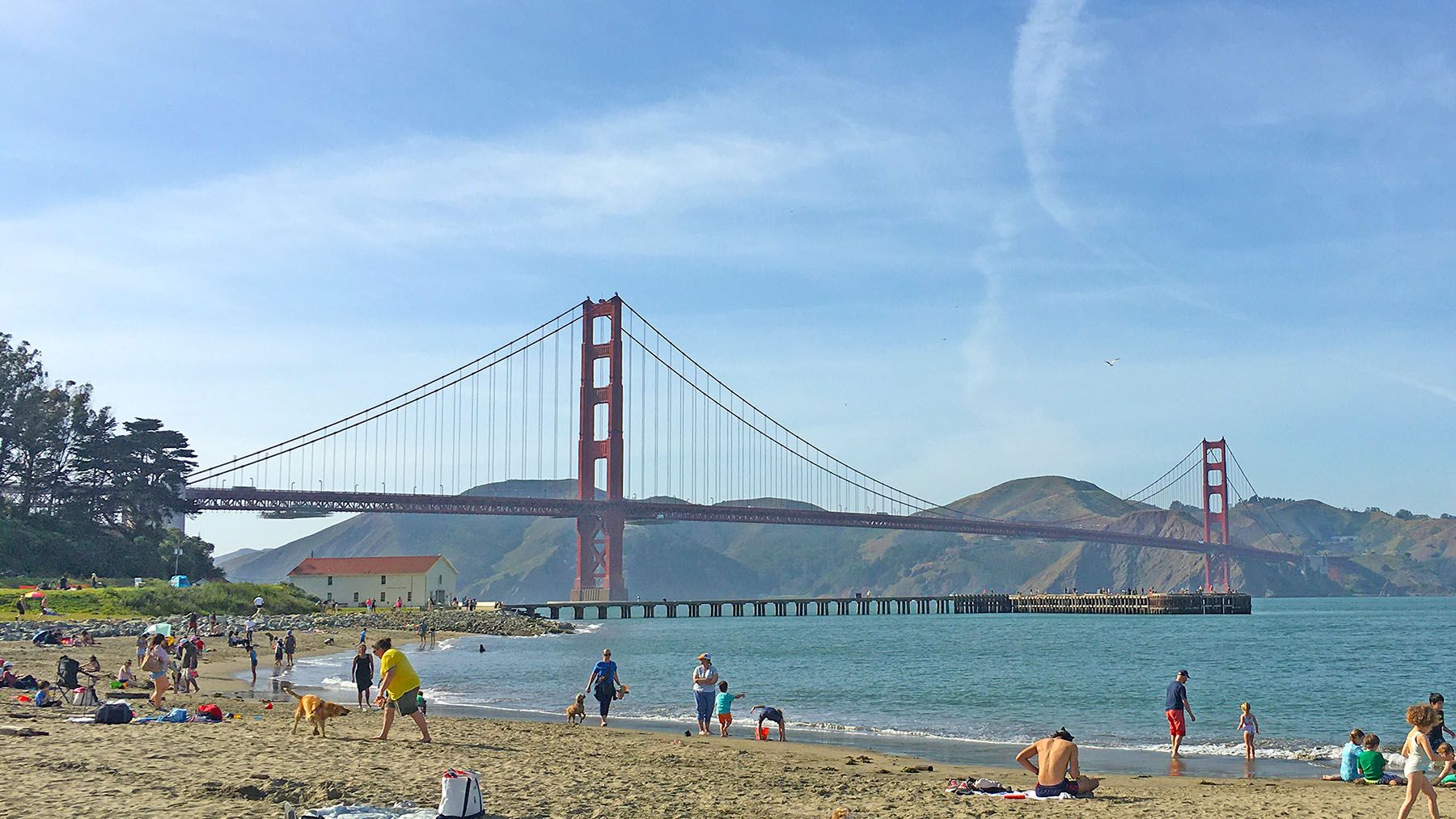 The Golden Gate Bridge. In the far background, rolling green hills, in the foreground, a sandy beach.