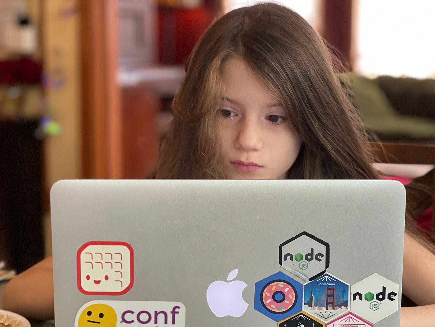 A young girl is working intently at her laptop, which is decorated with Node.js stickers.