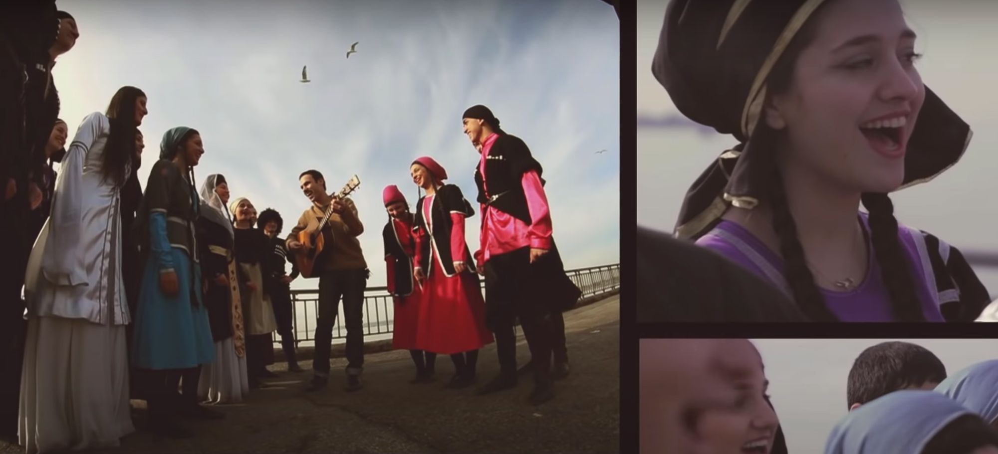 Dancers in traditional Georgian dress surround Ilusha Tsinadze, who is playing guitar and singing.