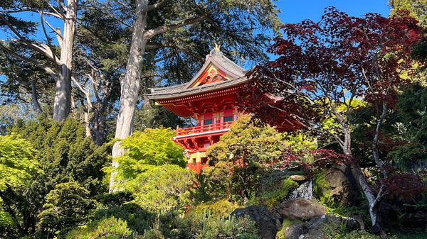 A Japanese structure, brightly painted red with a peaked roof, overlooks a manicured garden.